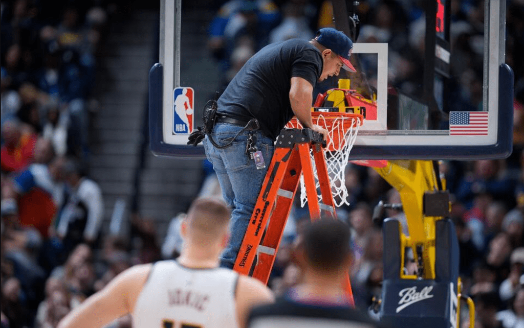 A worker uses a level to check the rim after it was bent by a dunk by Boston Celtics center Robert Williams III in the second half of an NBA basketball game against the Denver Nuggets.